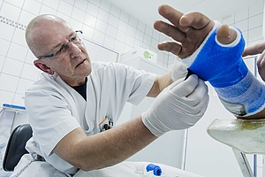 Bild zeigt einen Arzt, der einen Verband an der rechten Hand eines Patienten anbringt