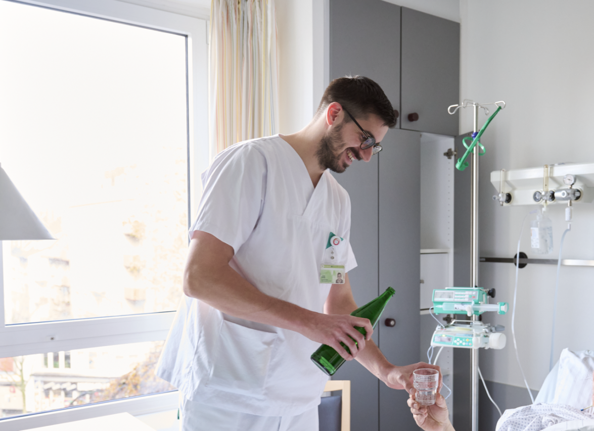 Ein Pfleger versorgt einen Patienten mit Mineralwasser.